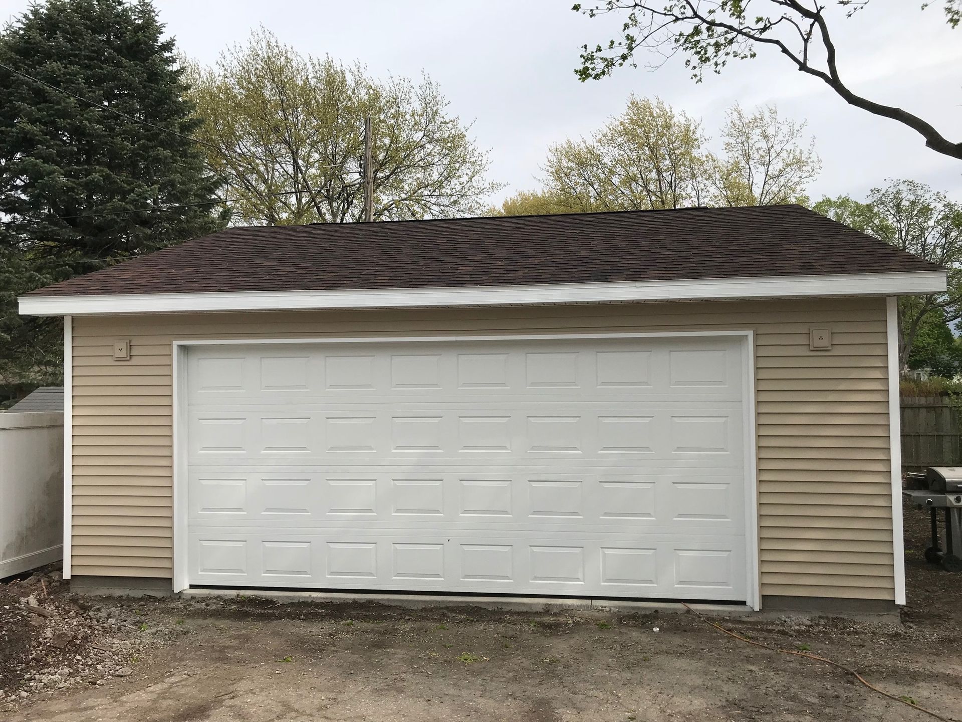 Detached beige garage with white double doors and dark shingled roof.