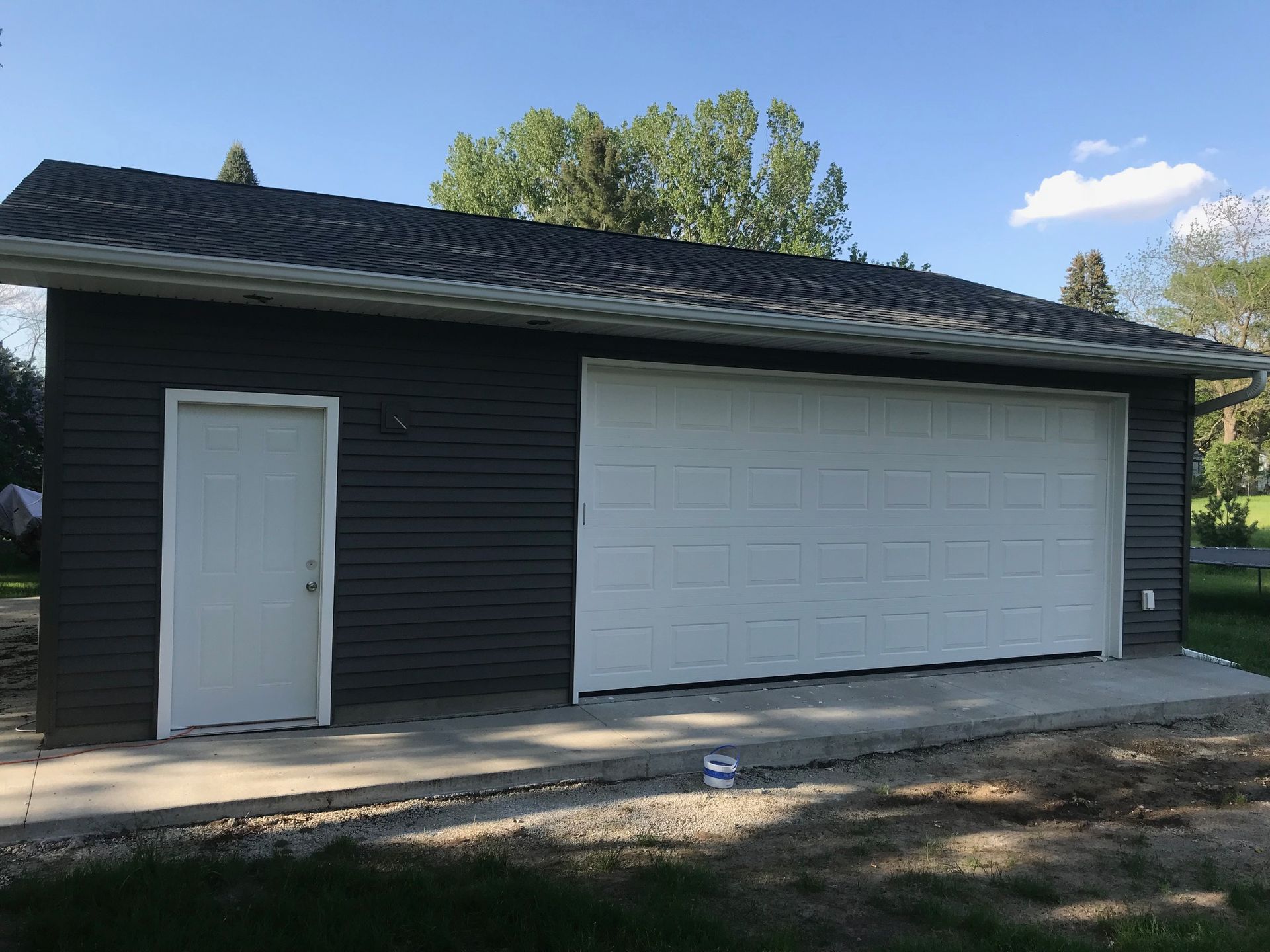 Dark garage building with a white side door and large white roll-up door under a blue sky