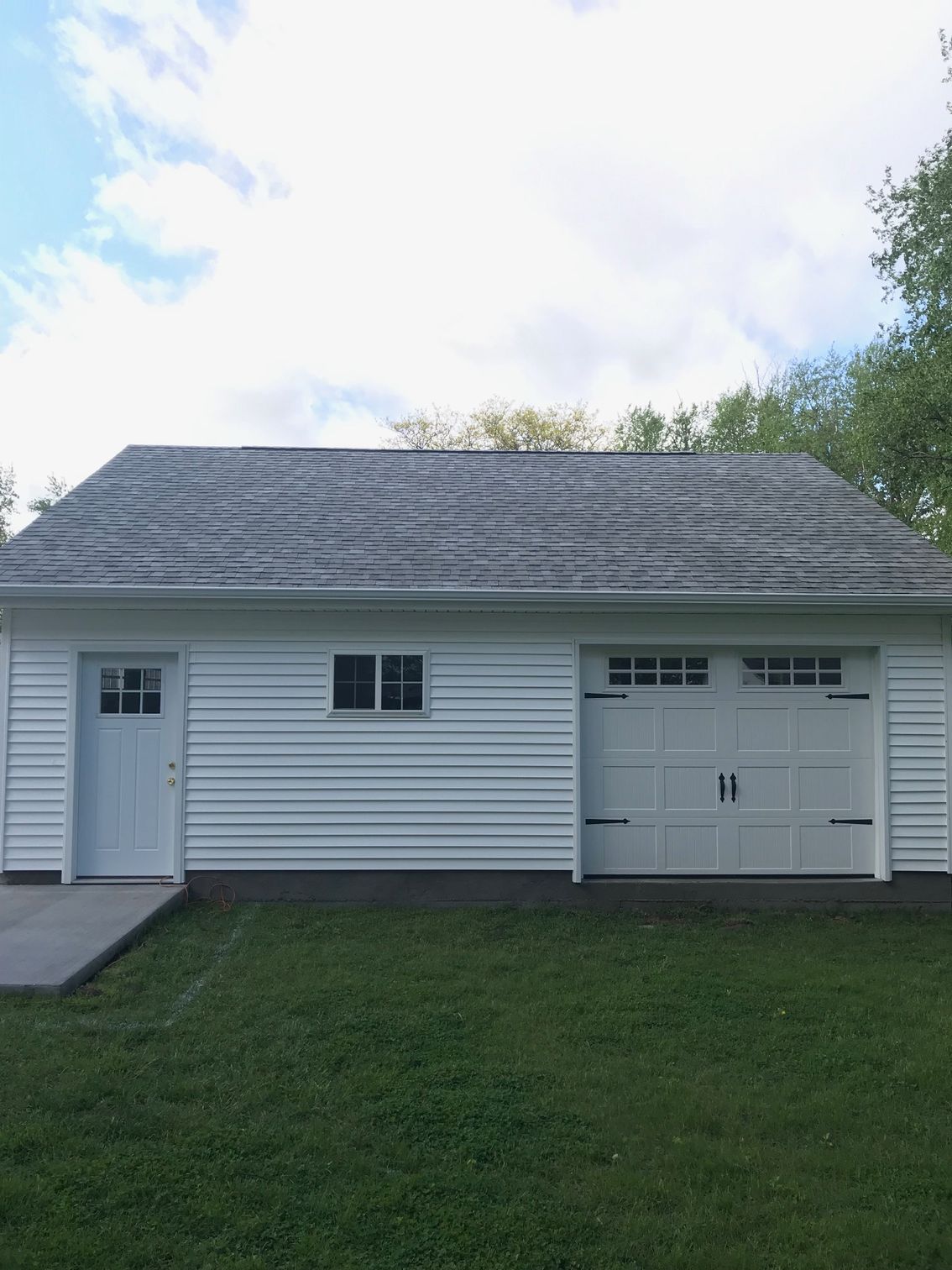 Small white garage with two doors, a side entry door, and a grassy lawn under a partly cloudy sky