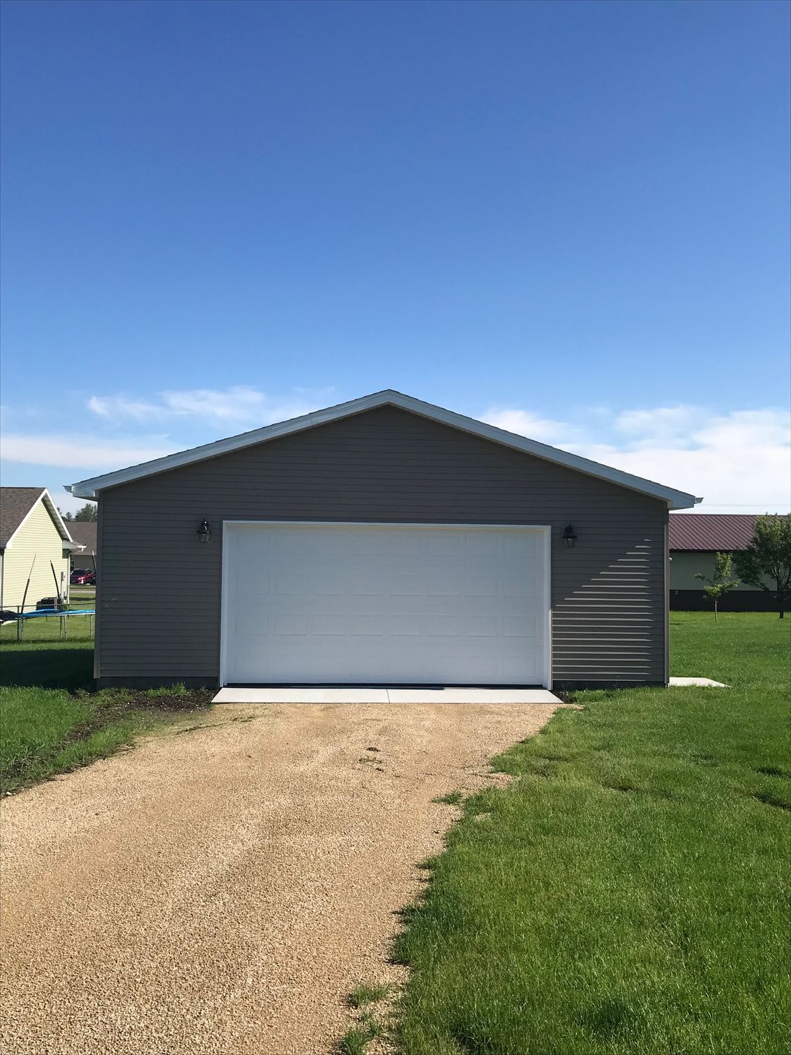 Detached gray garage with white door and gravel driveway under a clear blue sky