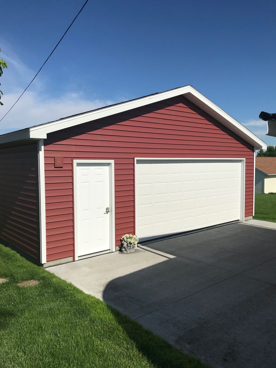 Red garage with white door and trim, beside a driveway and lawn under a clear blue sky.