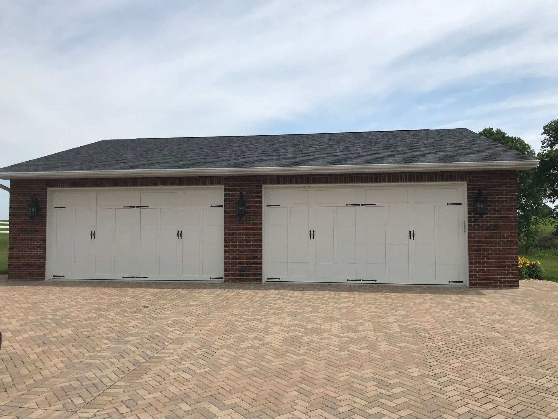 Two white garage doors on a brick outbuilding with a paved driveway under a blue sky