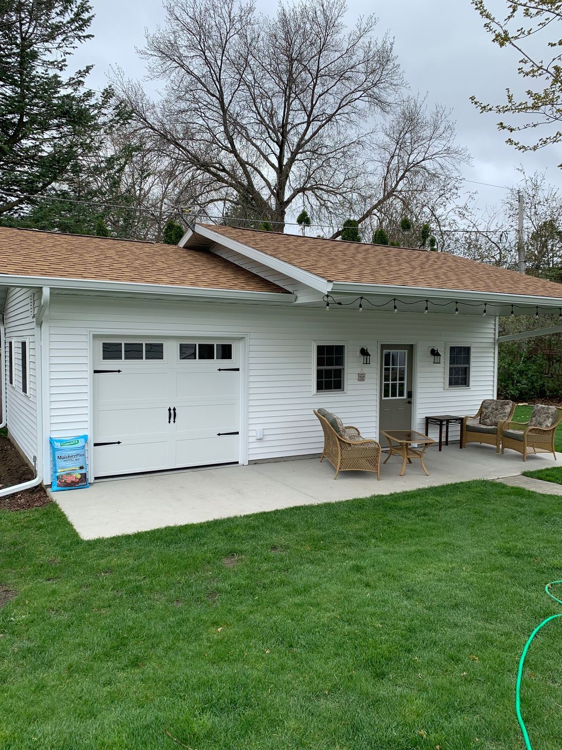 White house exterior with garage, patio chairs, and green lawn under a cloudy sky