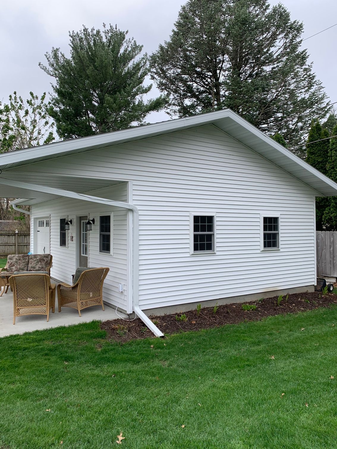 White house exterior with a covered patio, wicker chairs, and a green lawn in front.