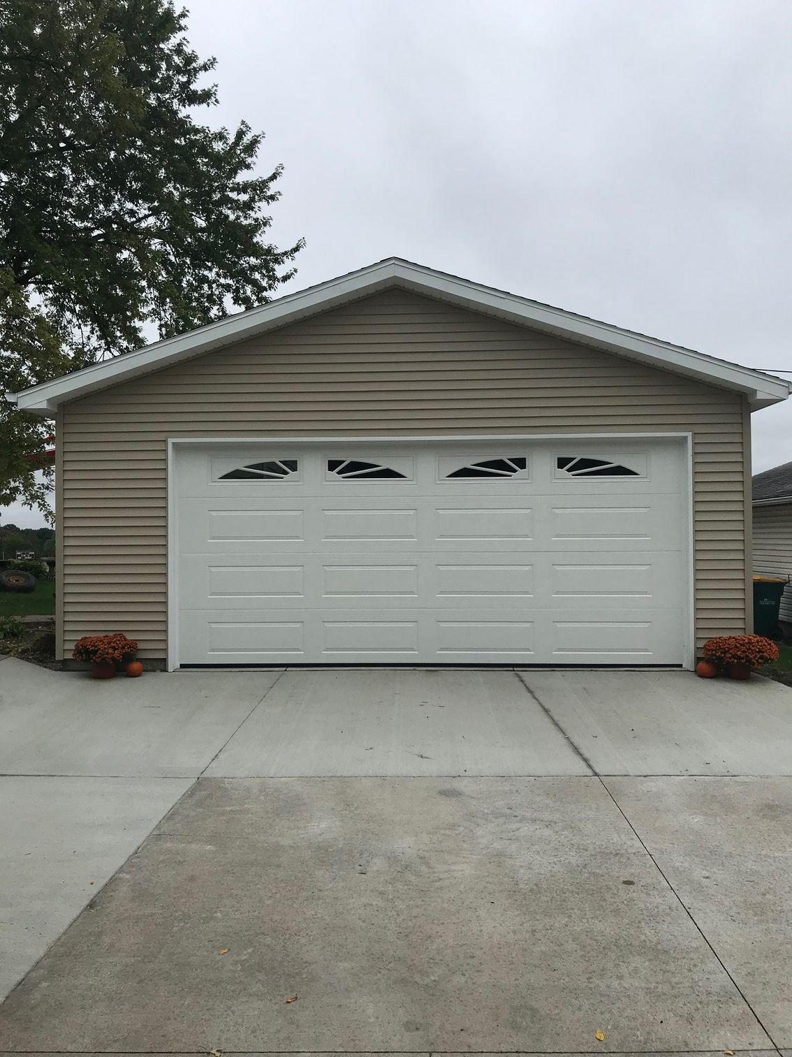 Single-car garage with a white door, beige siding, and concrete driveway under an overcast sky