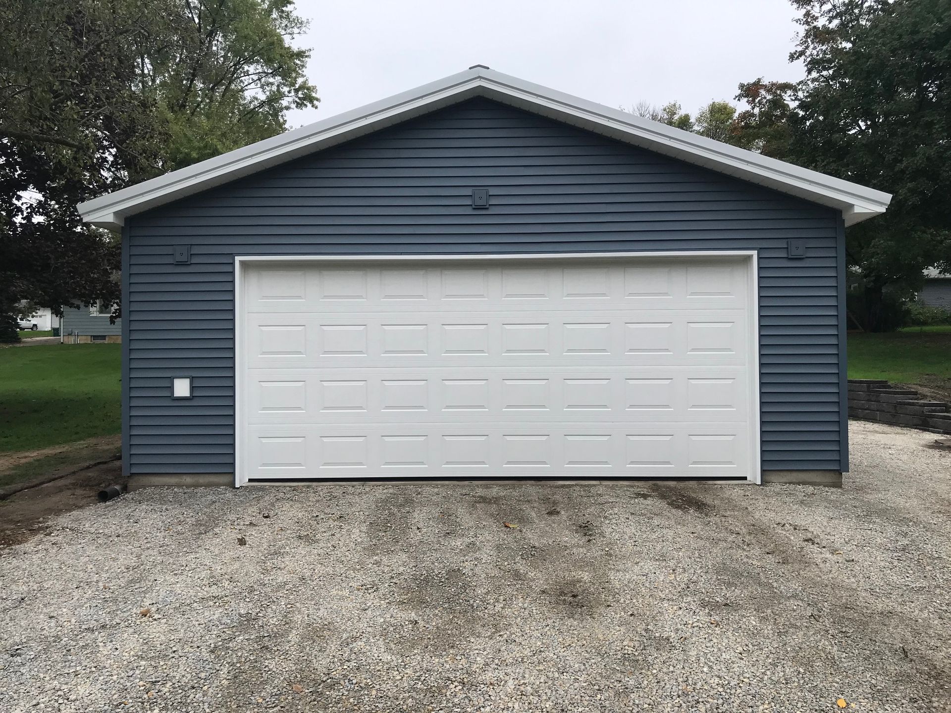 Blue garage with a white door and gravel driveway, viewed from the front.