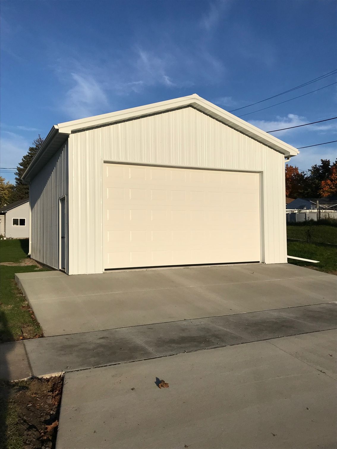 White metal garage with large closed door beside a concrete driveway under a blue sky.