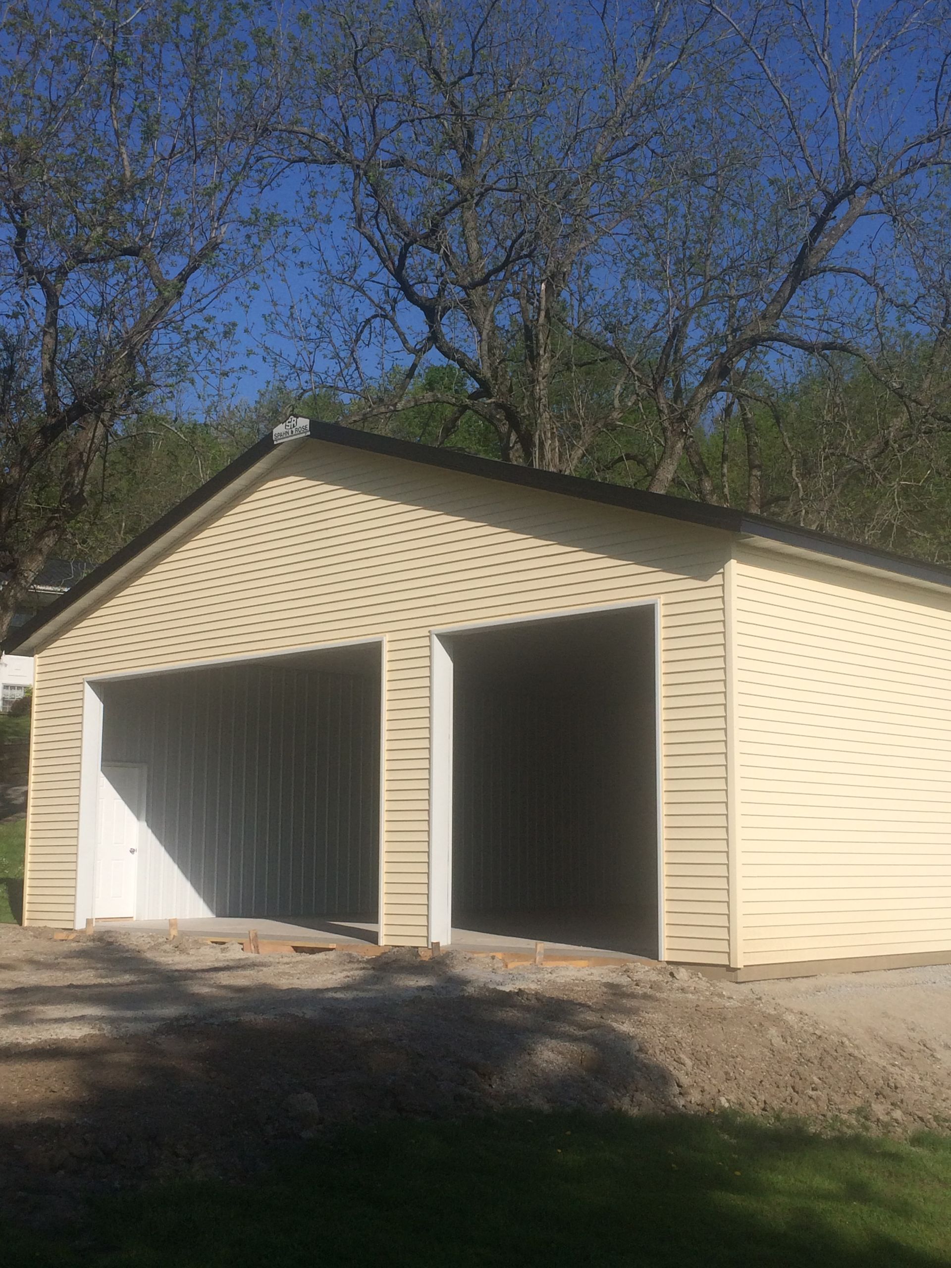 Two-car garage with beige siding and open doors under trees on a sunny day