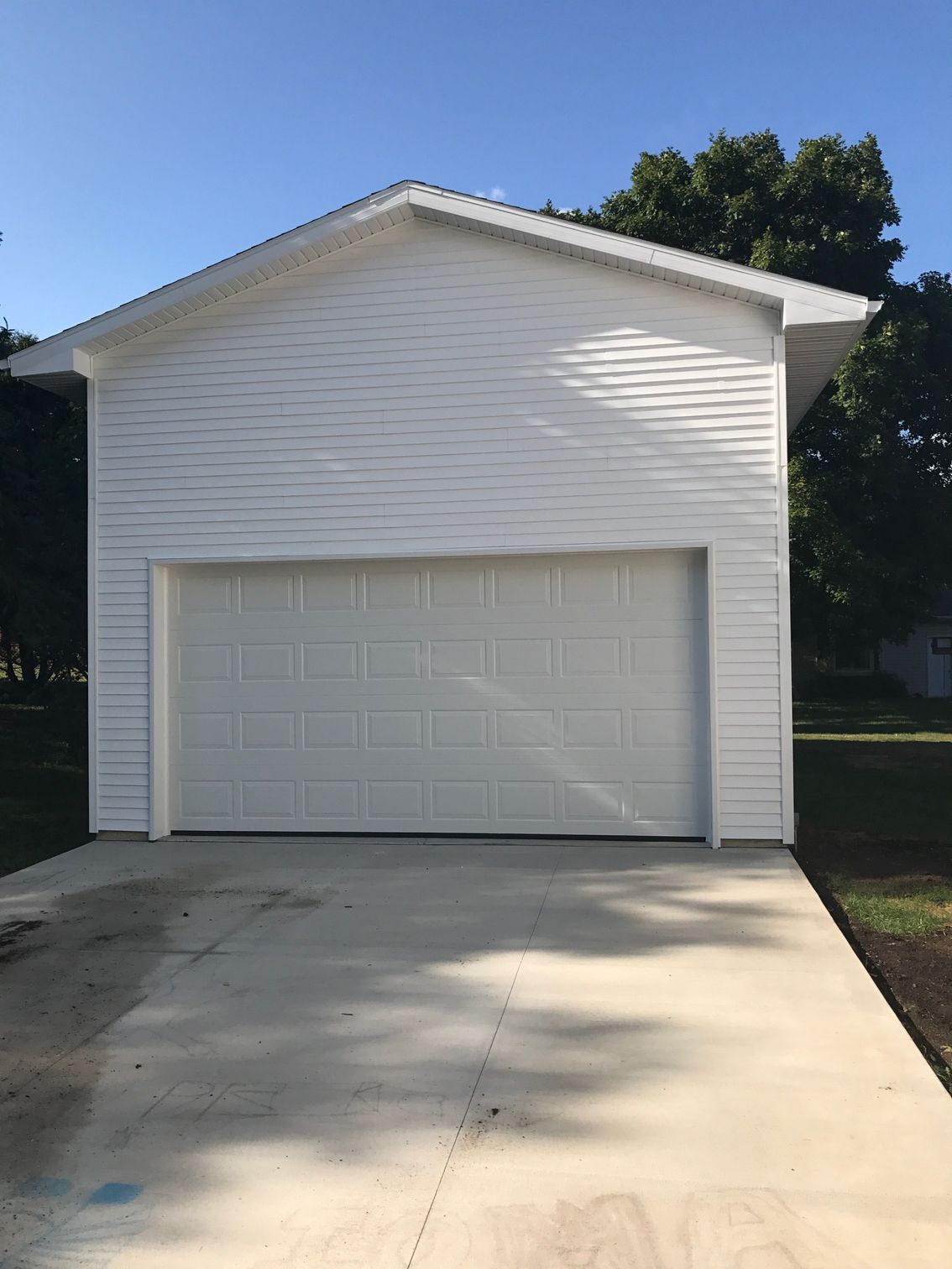 White detached garage with a concrete driveway and trees in the background