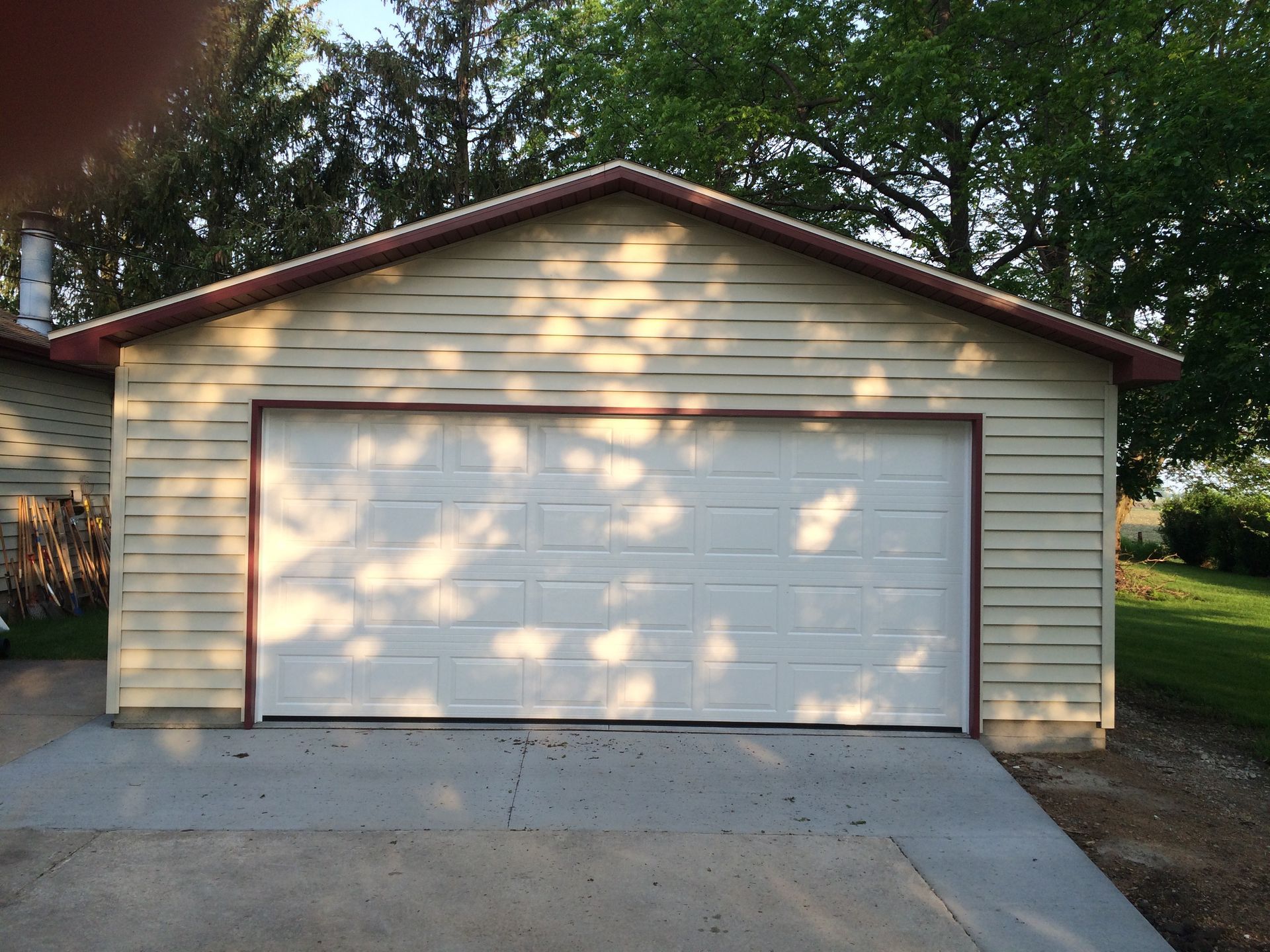 Detached beige garage with white door and concrete driveway in a wooded yard