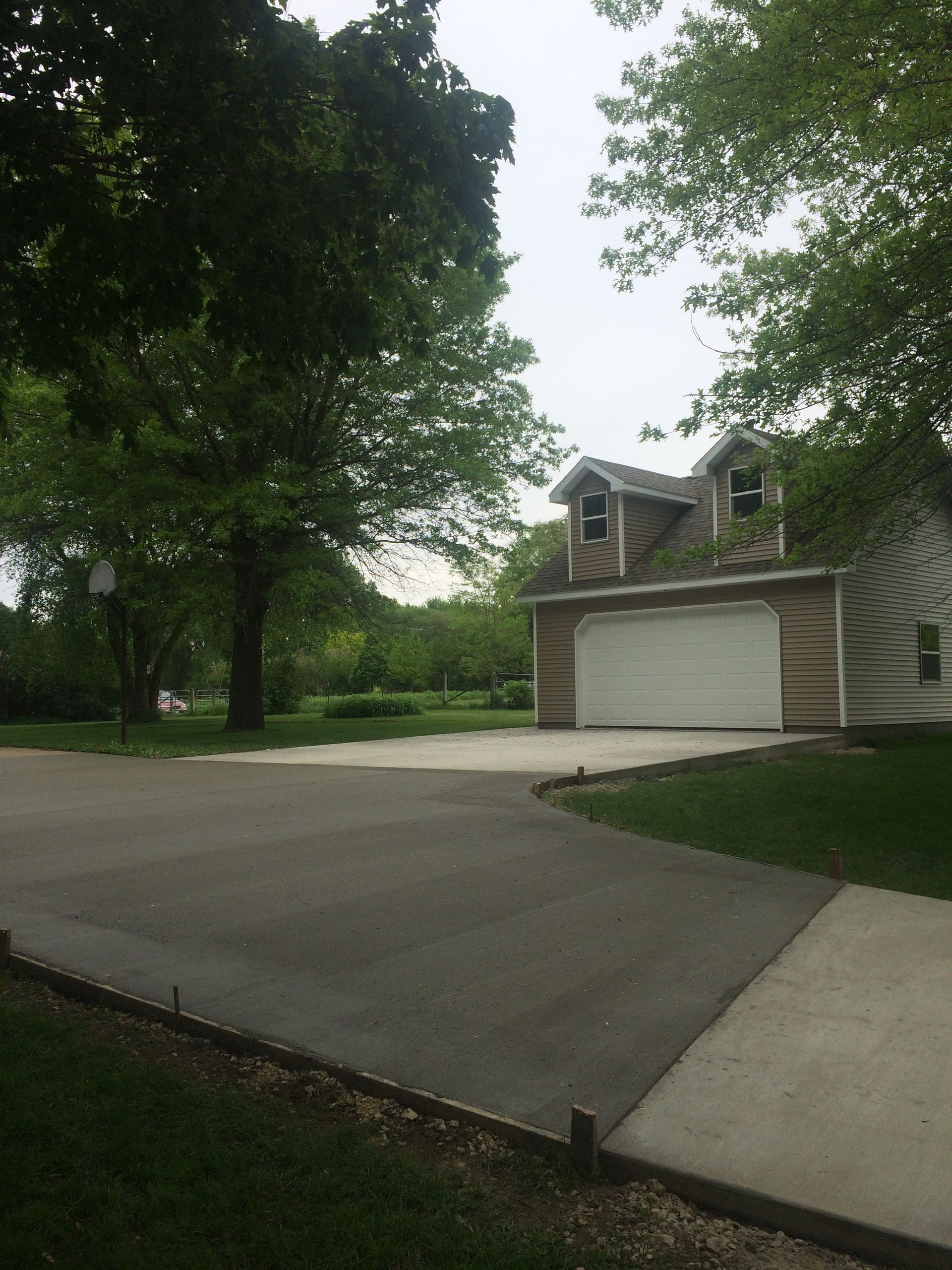 Driveway leading to a two-car garage beside a leafy suburban house on an overcast day