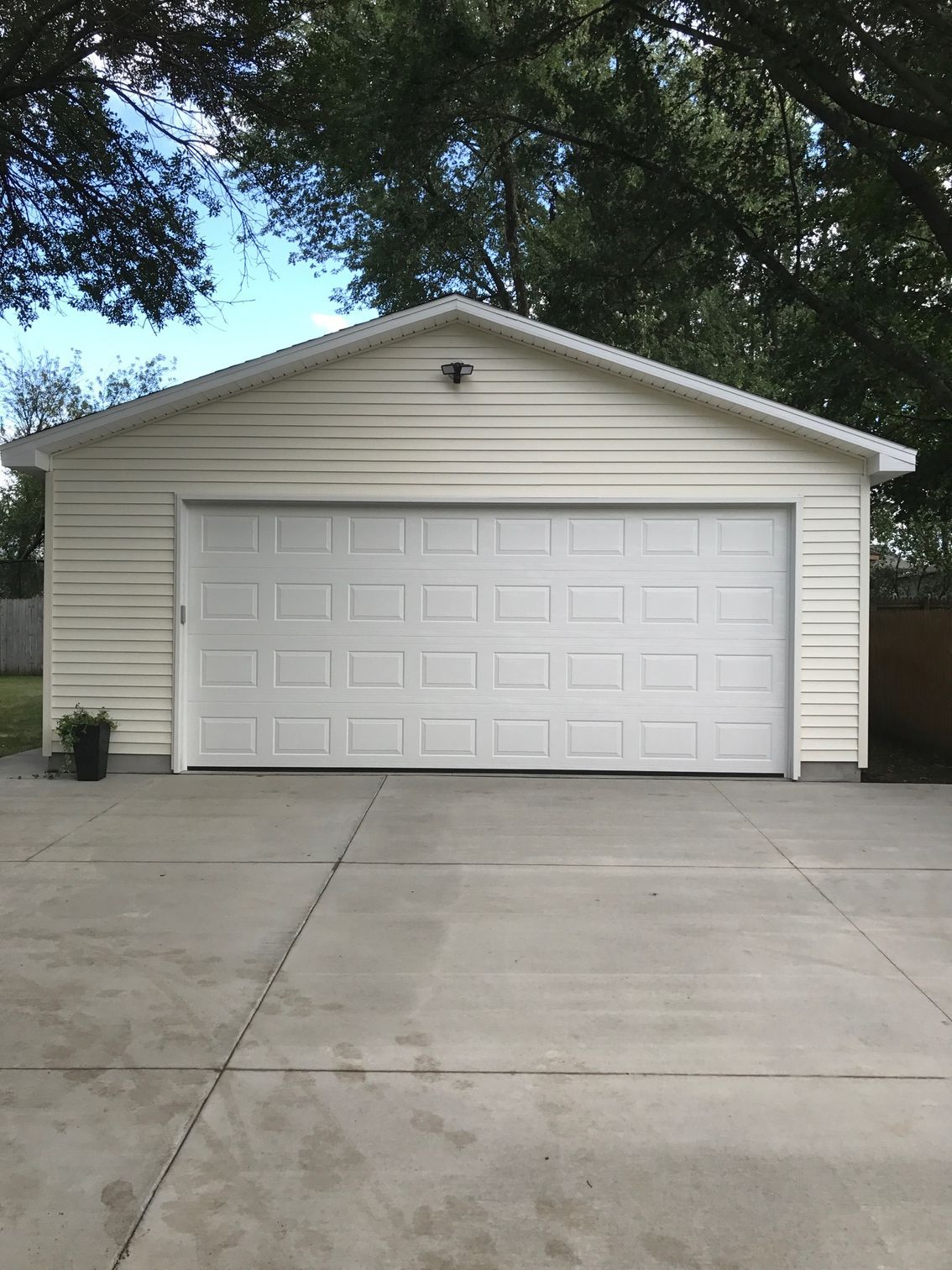 Detached beige garage with white double doors and a concrete driveway under trees