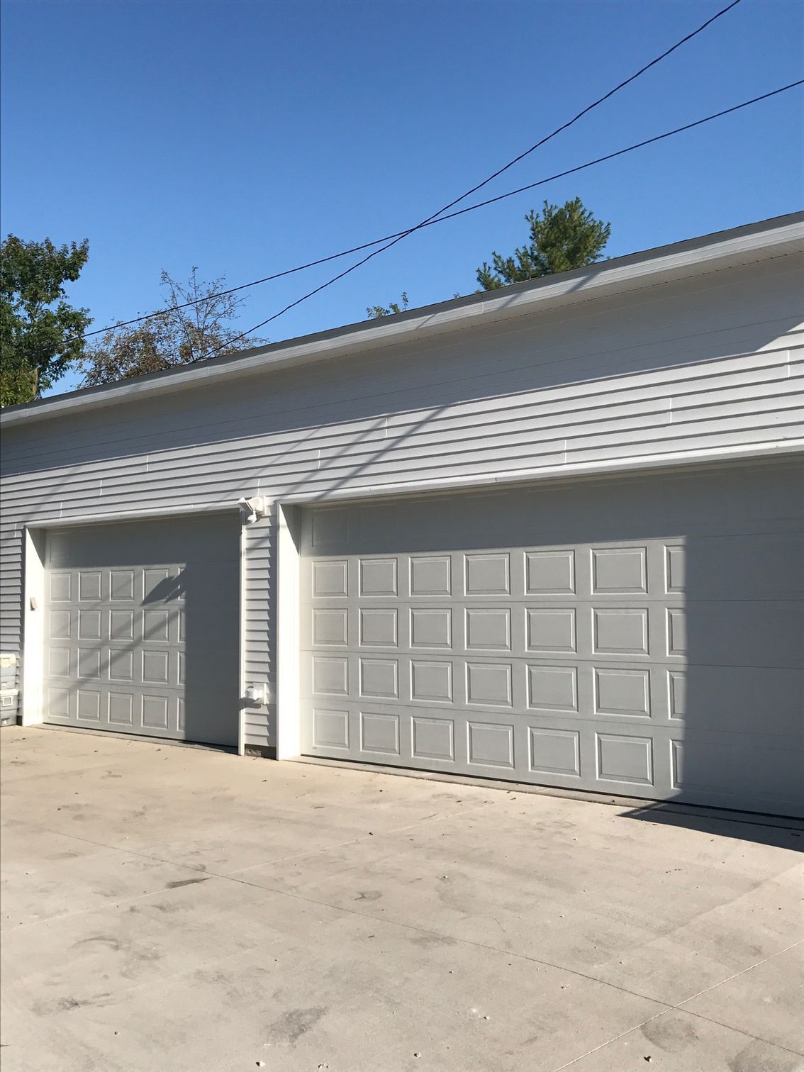 Two white garage doors on a light gray building under a blue sky.