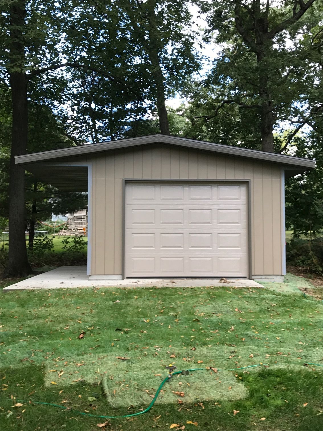 Small beige garage with a closed door, surrounded by trees and grass.