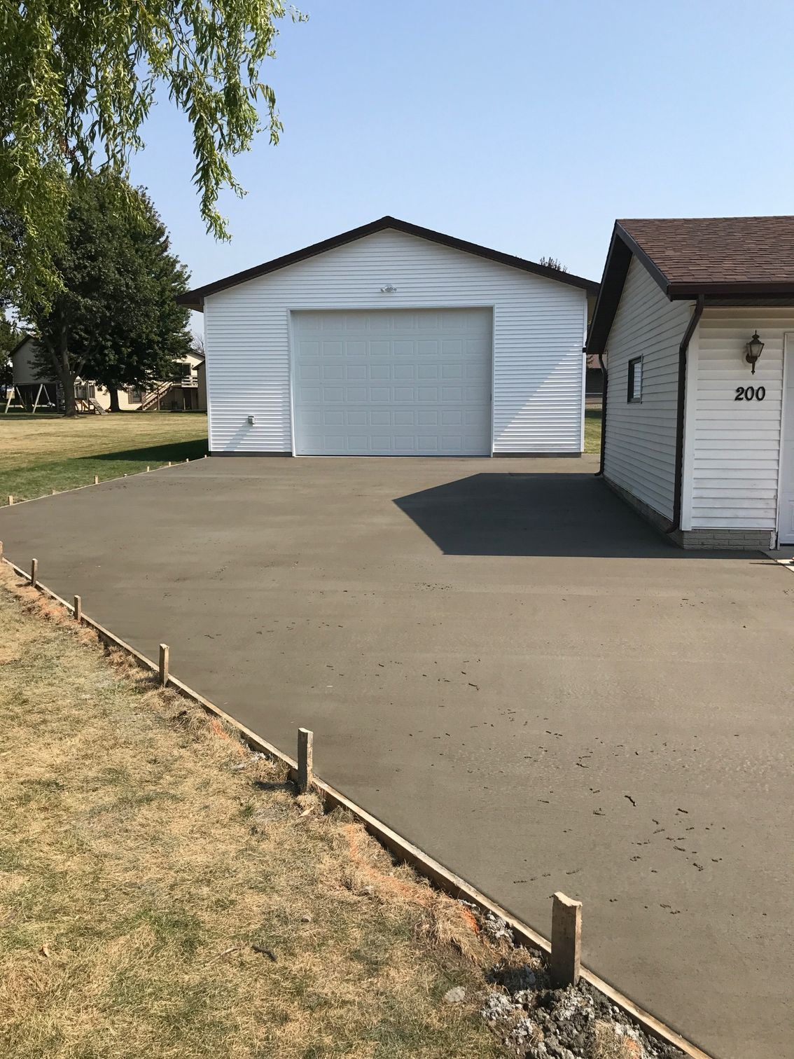 White detached garage with closed door and wide paved driveway beside a grassy yard.