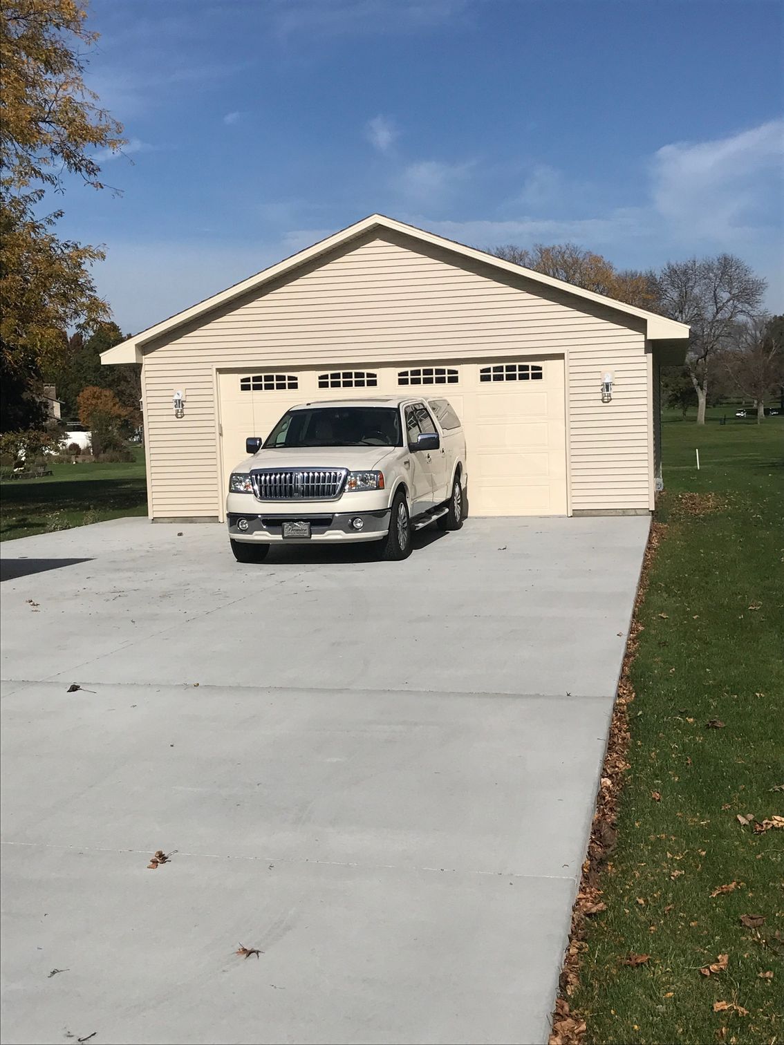 White SUV parked on a long driveway in front of a beige garage under a blue sky