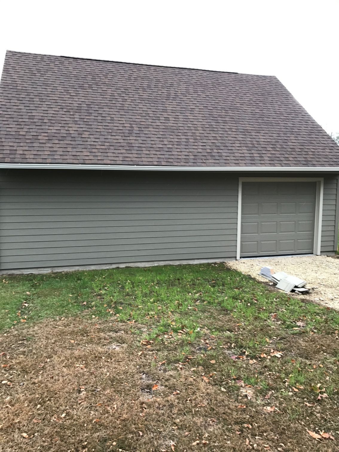 Gray garage with a shingled roof and a patchy grass front yard
