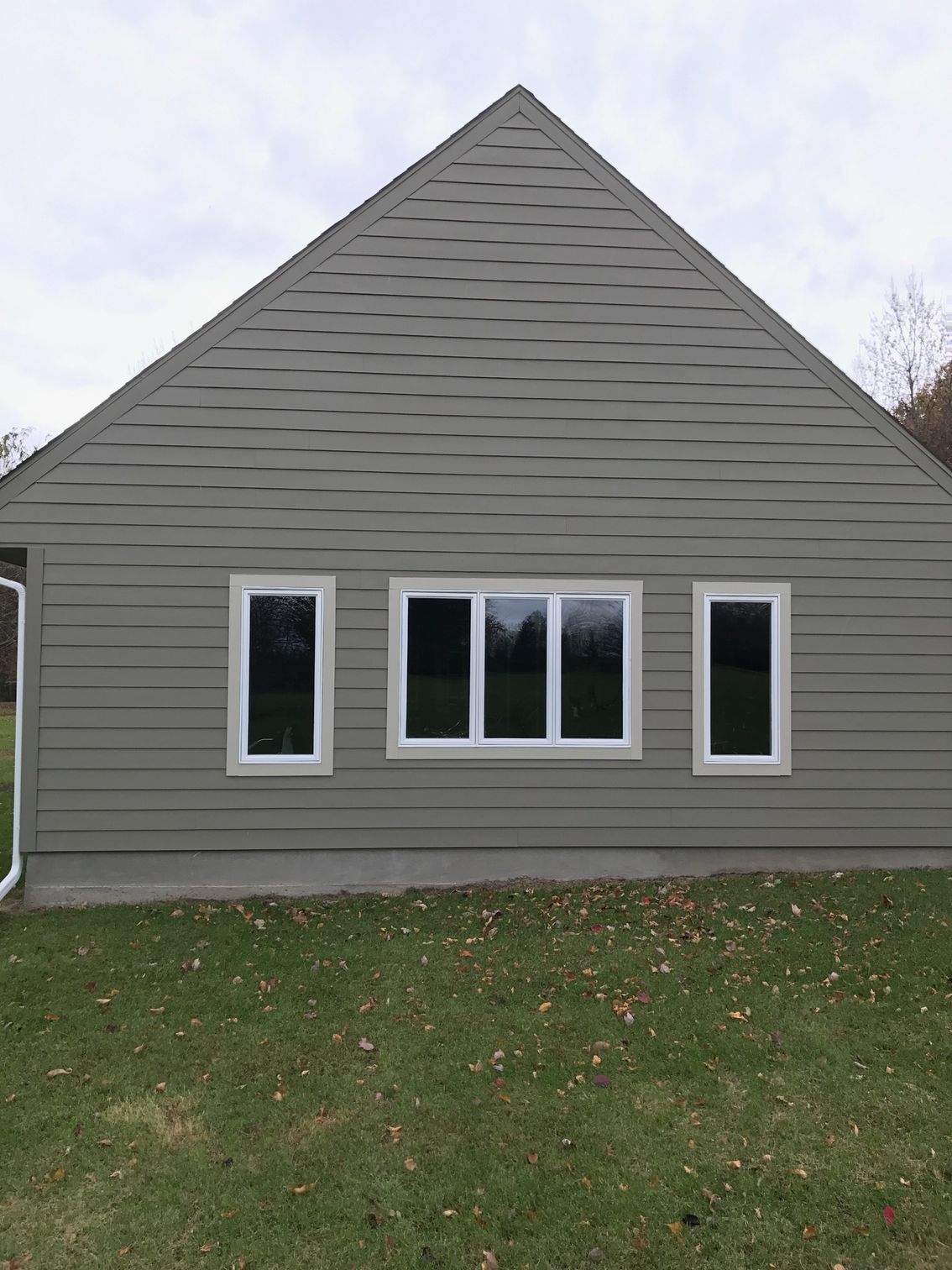 Gray house exterior with three windows and a green lawn under an overcast sky
