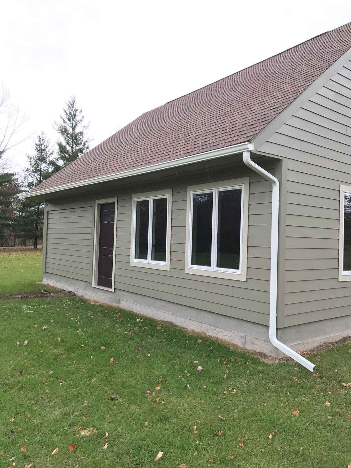 Gray house exterior with white-trim windows and a brown shingled roof