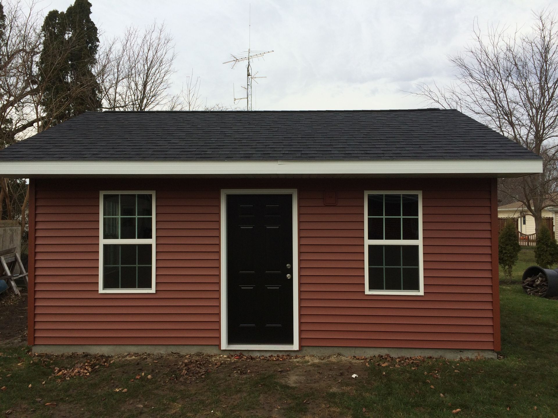 Small red cabin with black roof, white-trim windows, and a centered front door in a yard