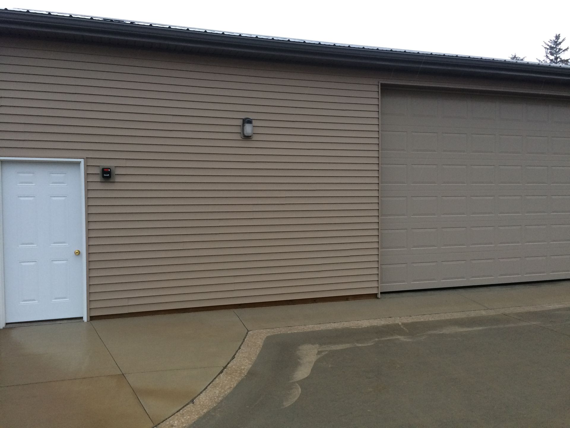 Exterior of a beige industrial building with a white door and gray garage door on a wet pavement
