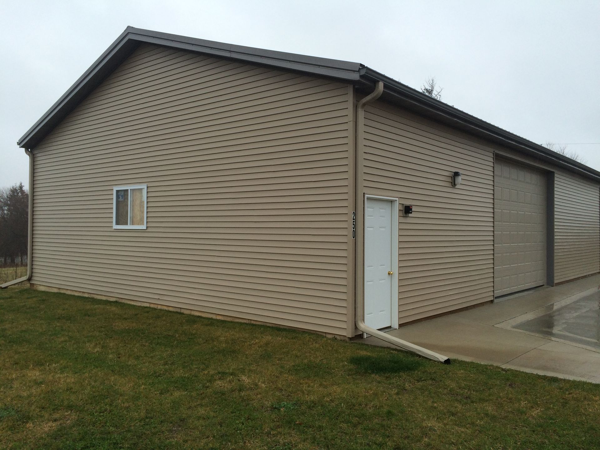 Tan siding house with a white door, small window, and concrete driveway on a grassy lot
