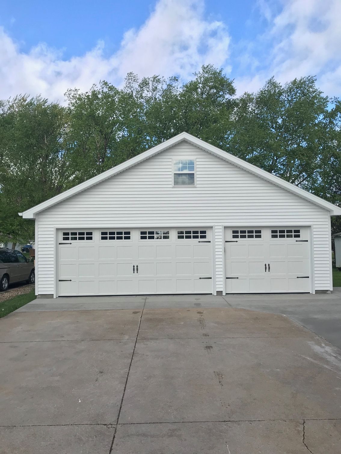 White two-car garage with three white doors and a concrete driveway under a cloudy sky