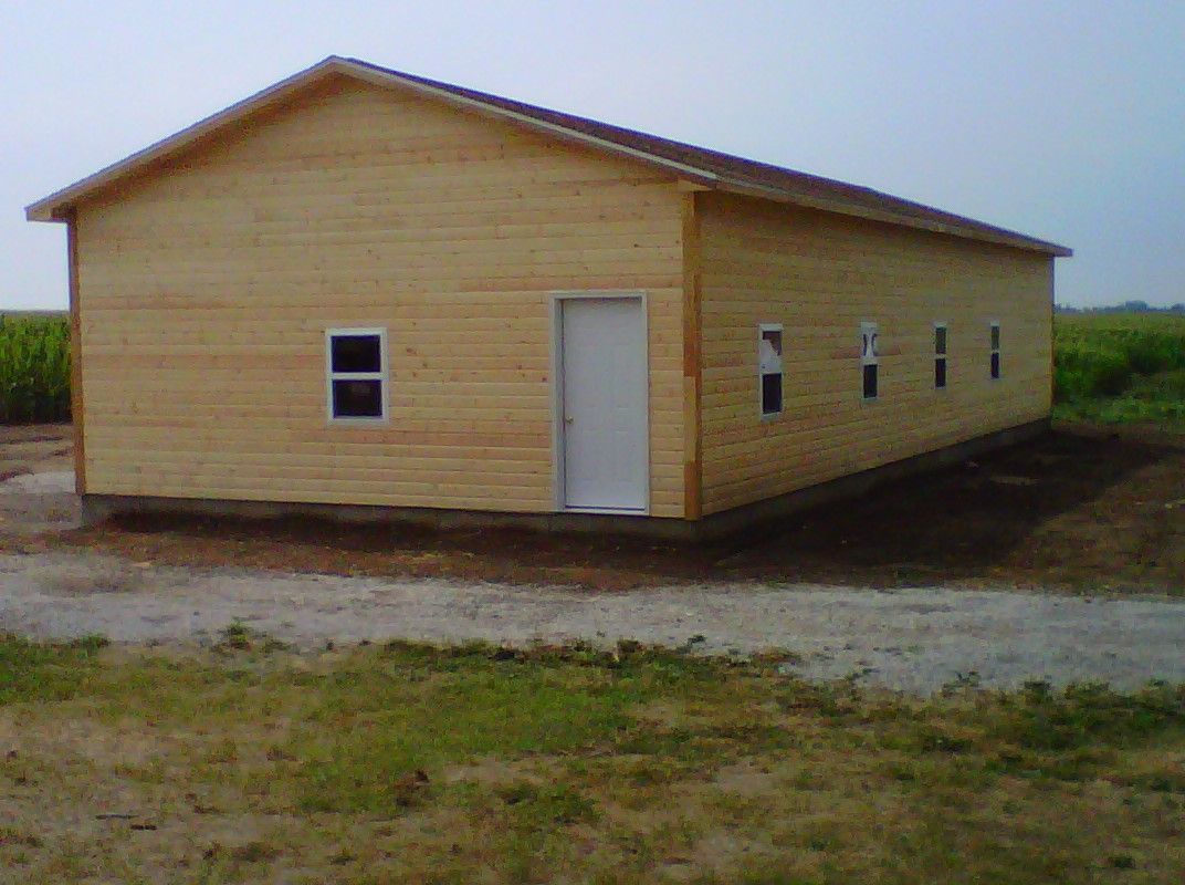 Small beige wooden building with a white door and windows on a gravel lot