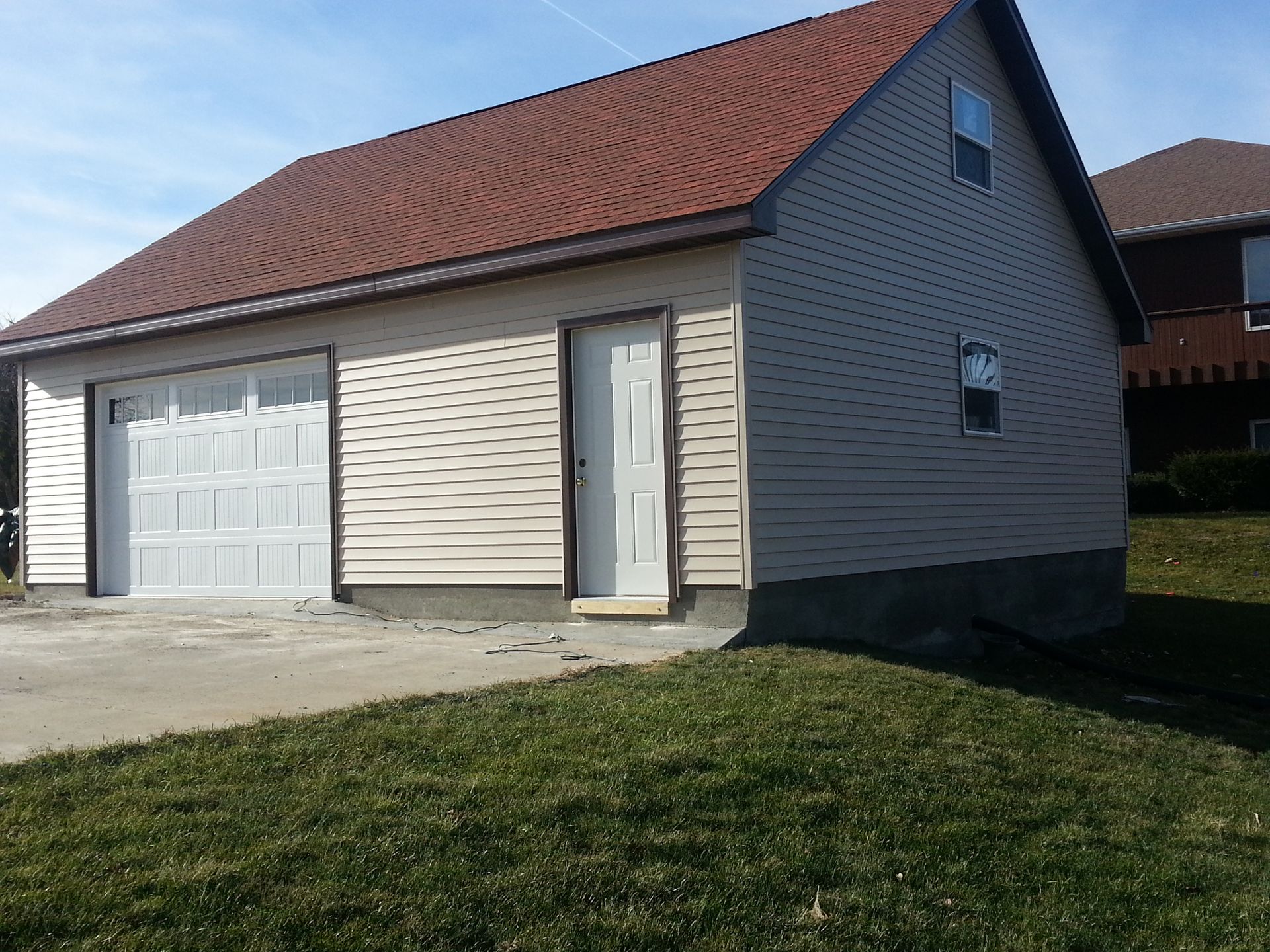 Detached beige house with red roof, white garage door, and small front entry on a sunny day
