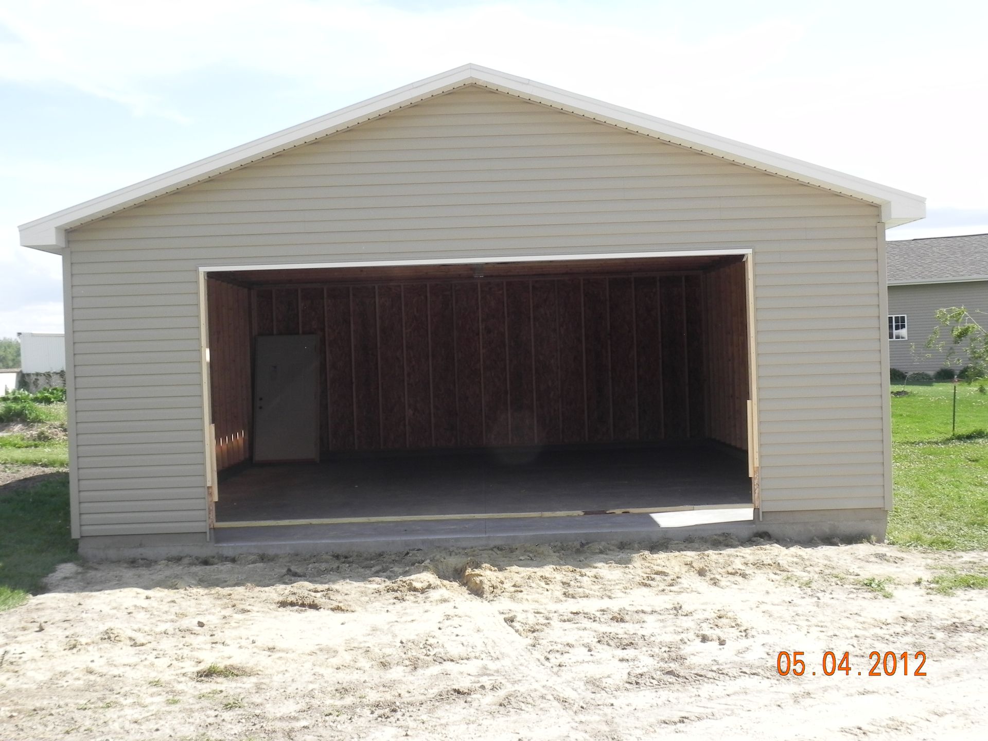 Front view of a beige detached garage with an open door, showing a dark interior and concrete driveway.