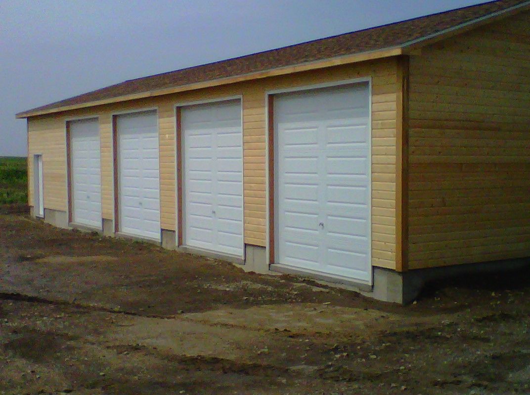 Row of white garage doors on a tan industrial building beside a muddy dirt lot