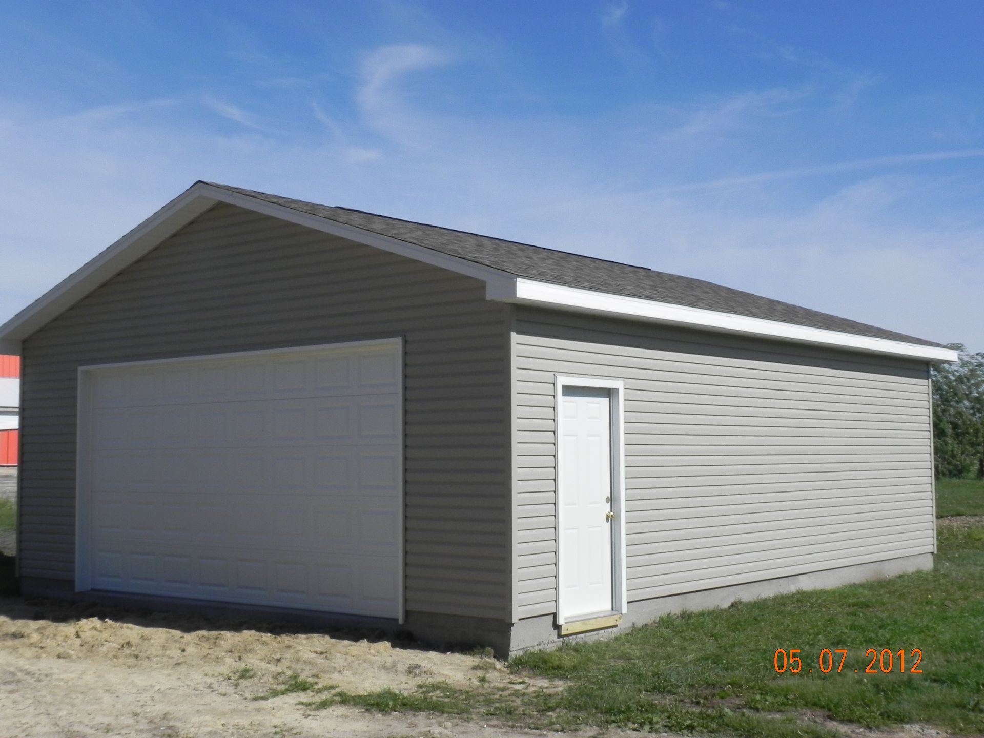 Gray detached garage with a white door and large roll-up door under a blue sky