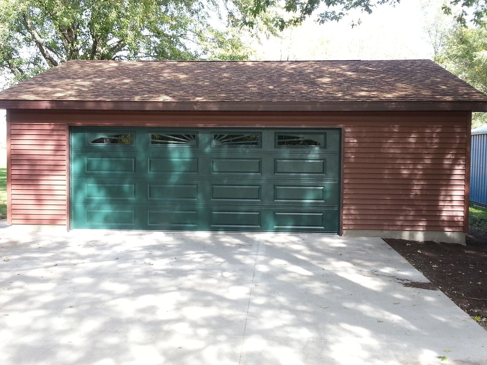 Two-car garage with teal doors and red siding, viewed from a sunlit driveway