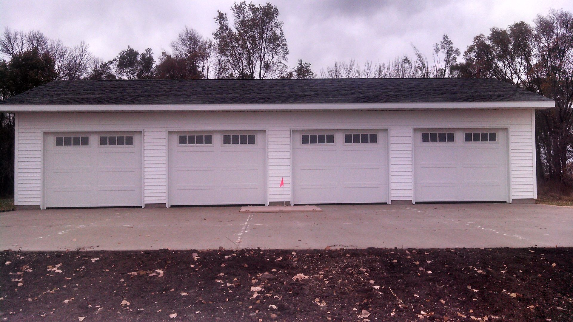 Four-car garage with white doors and a gray roof in a driveway, seen in overcast weather