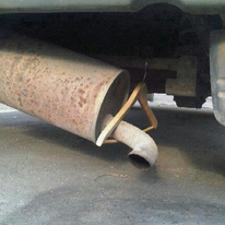 A rusty exhaust pipe with a wooden hanger attached to it