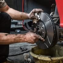 A man is cleaning a brake disc on a car in a garage.