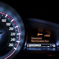 A close up of a car dashboard with a speedometer and a maintenance due notification.