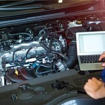 A person is working on a car engine with a laptop.