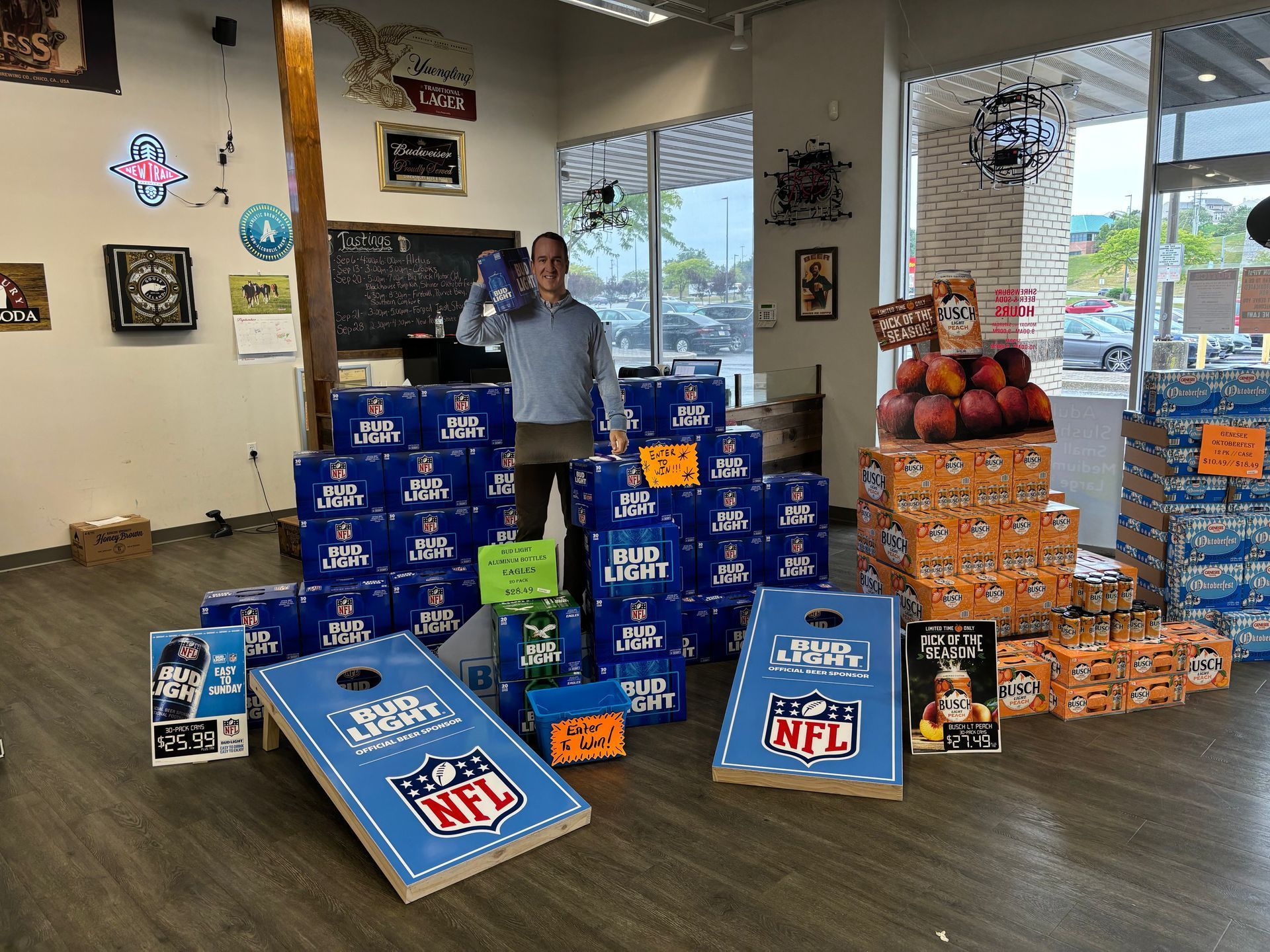 A man is standing in front of a pile of beer boxes and cornhole boards.