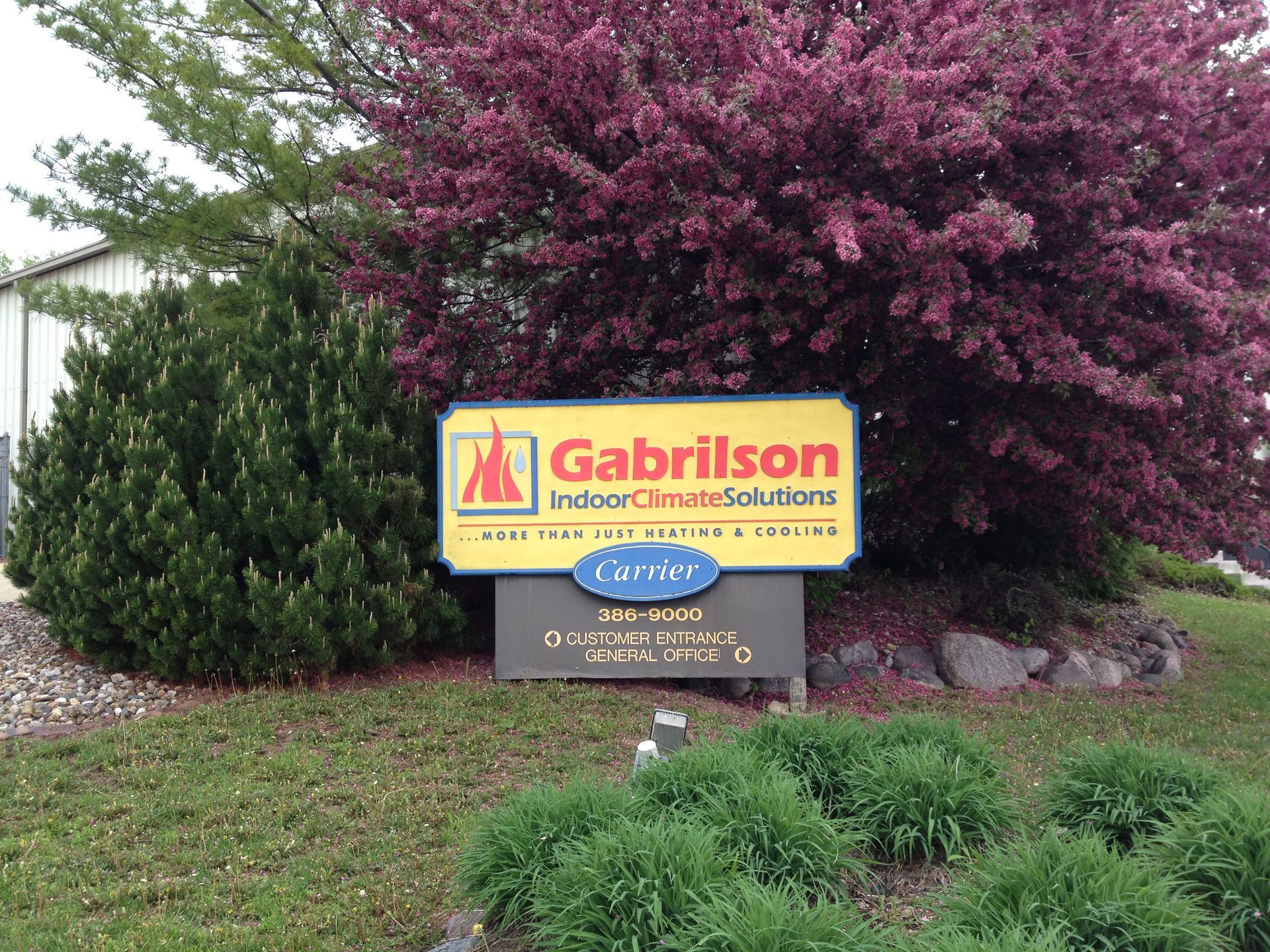 Sign for Gabrilson Interior Cleaning Solutions with colorful logo, in front of bushes.