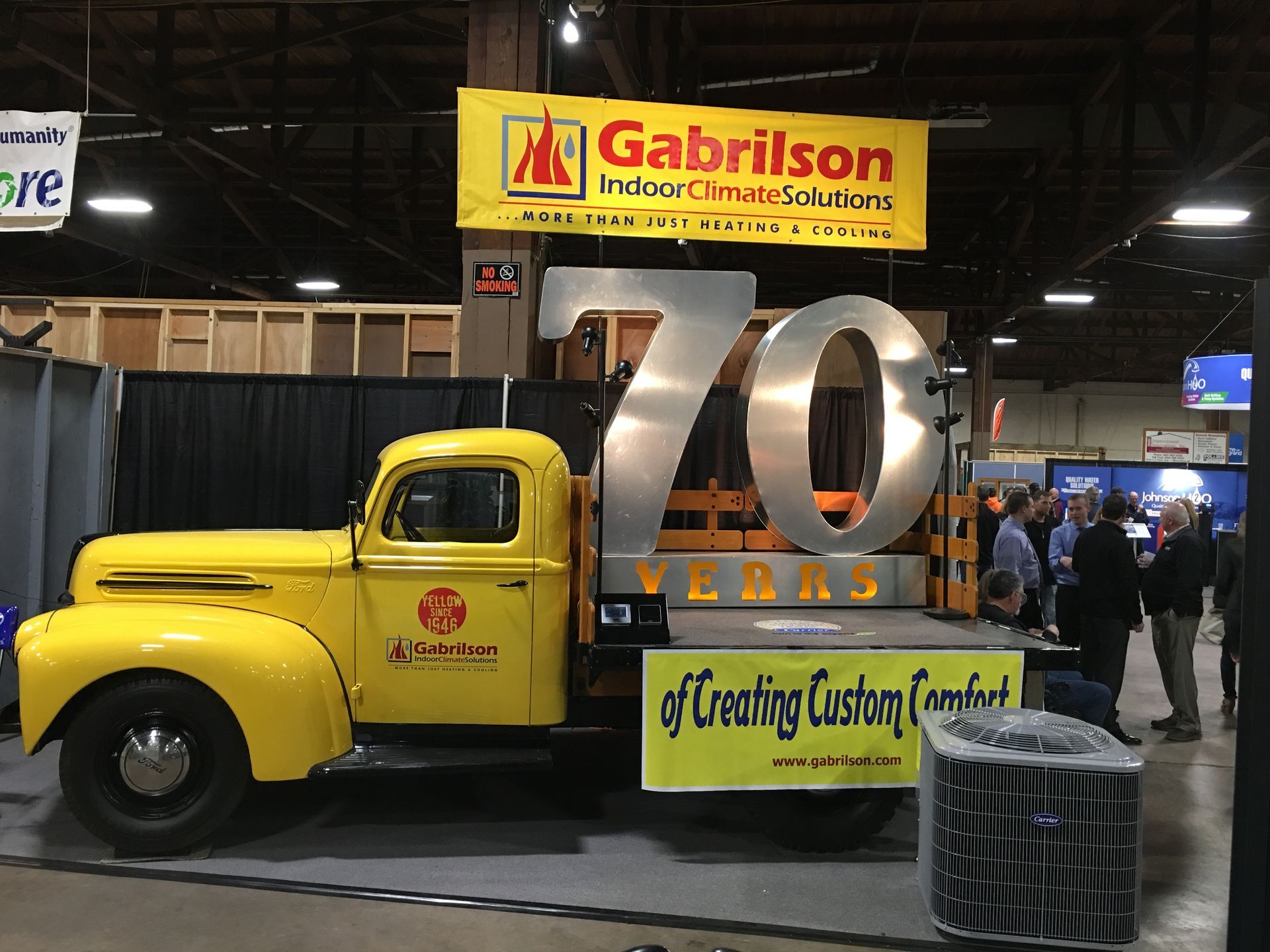 A bright yellow vintage truck at a trade show exhibit for Gabrilson, featuring a large 