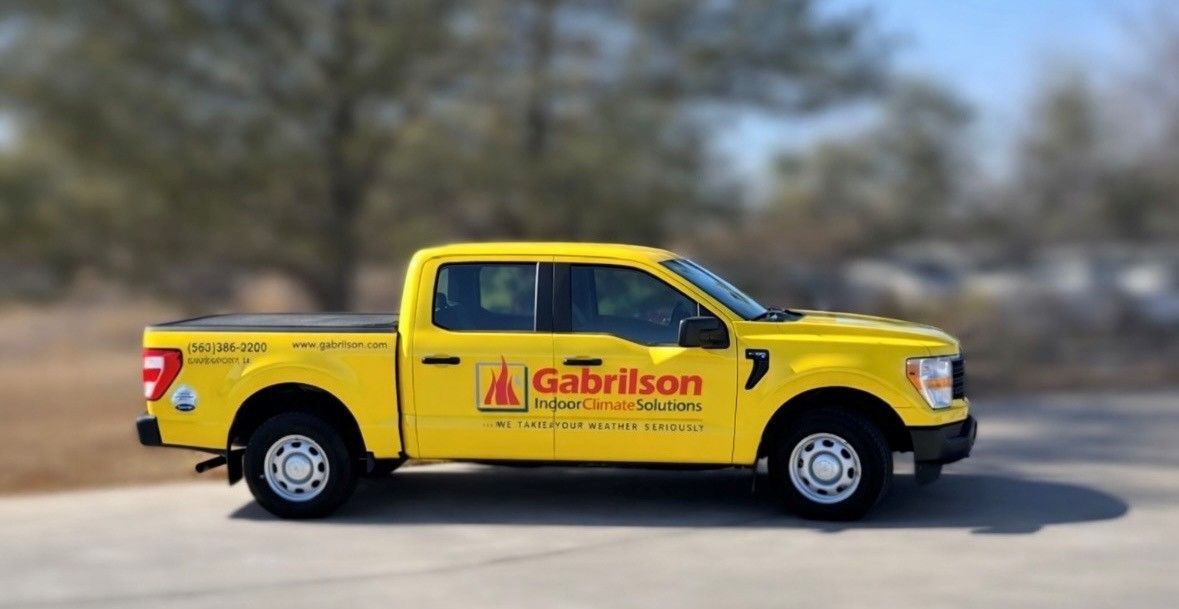 A bright yellow Gabrilson truck parked on an asphalt lot with a blurred background of trees.