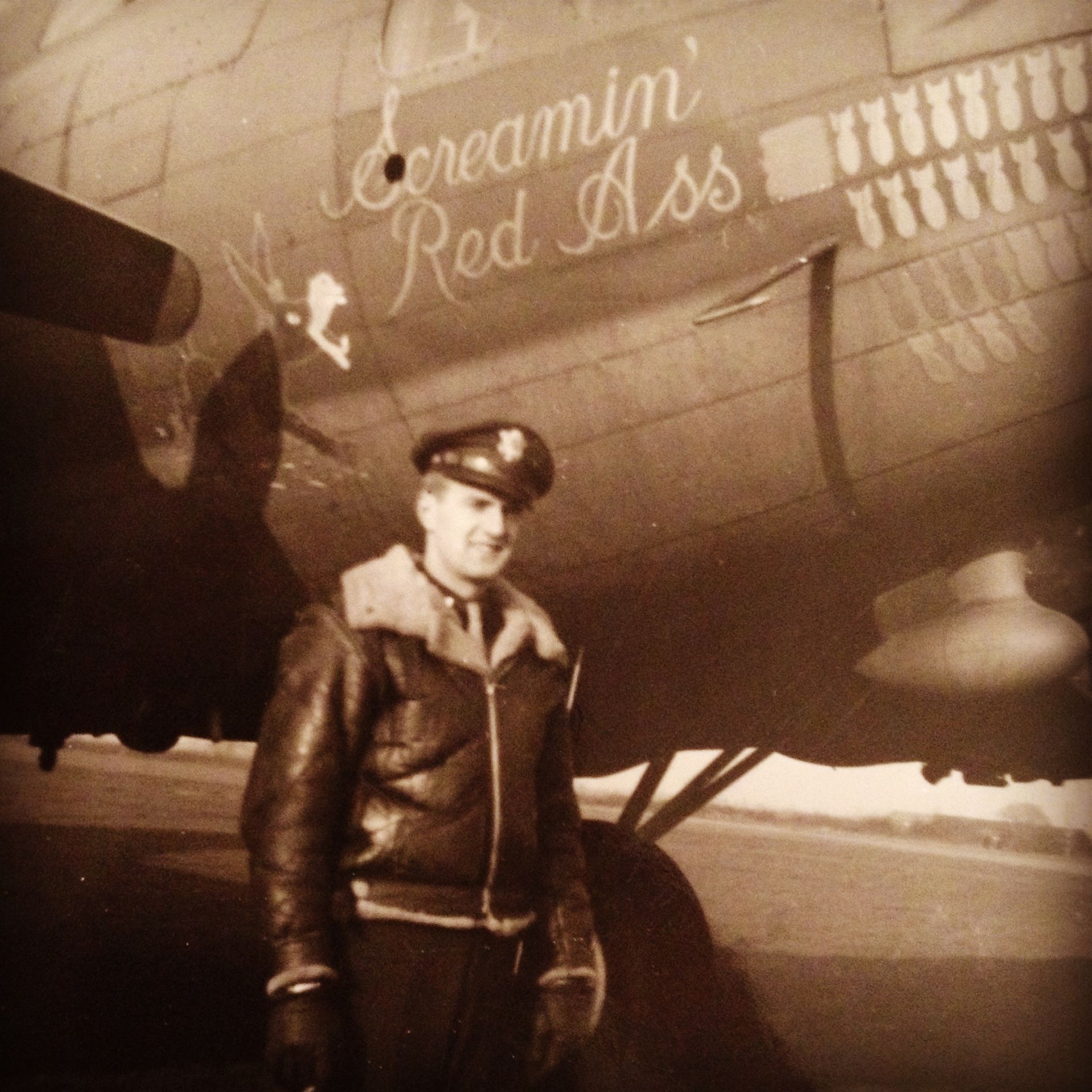 A pilot in a leather flight jacket standing in front of a B-17 bomber nose-art painted 