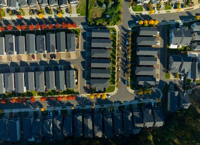 Aerial view of a residential neighborhood with rows of houses, trees, and parked cars along streets.