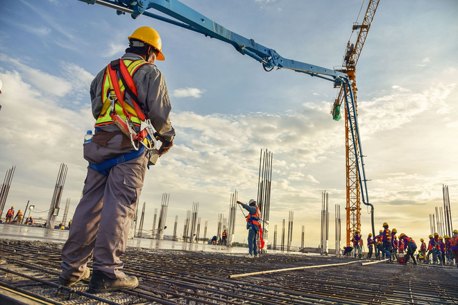 Construction workers on a building site with cranes and concrete slabs under a cloudy sky