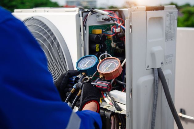 Technician servicing an outdoor air conditioner unit with pressure gauges attached