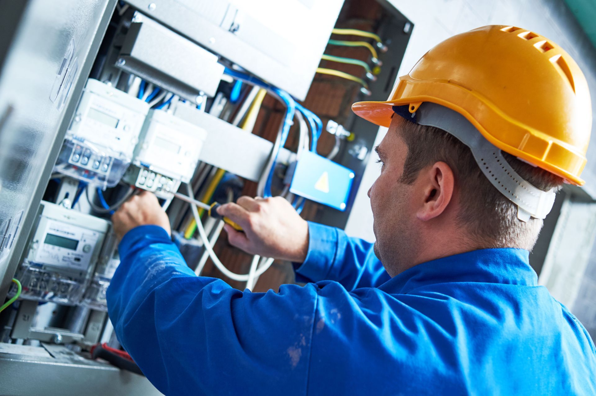 Technician in orange hard hat inspecting electrical wiring in a control panel