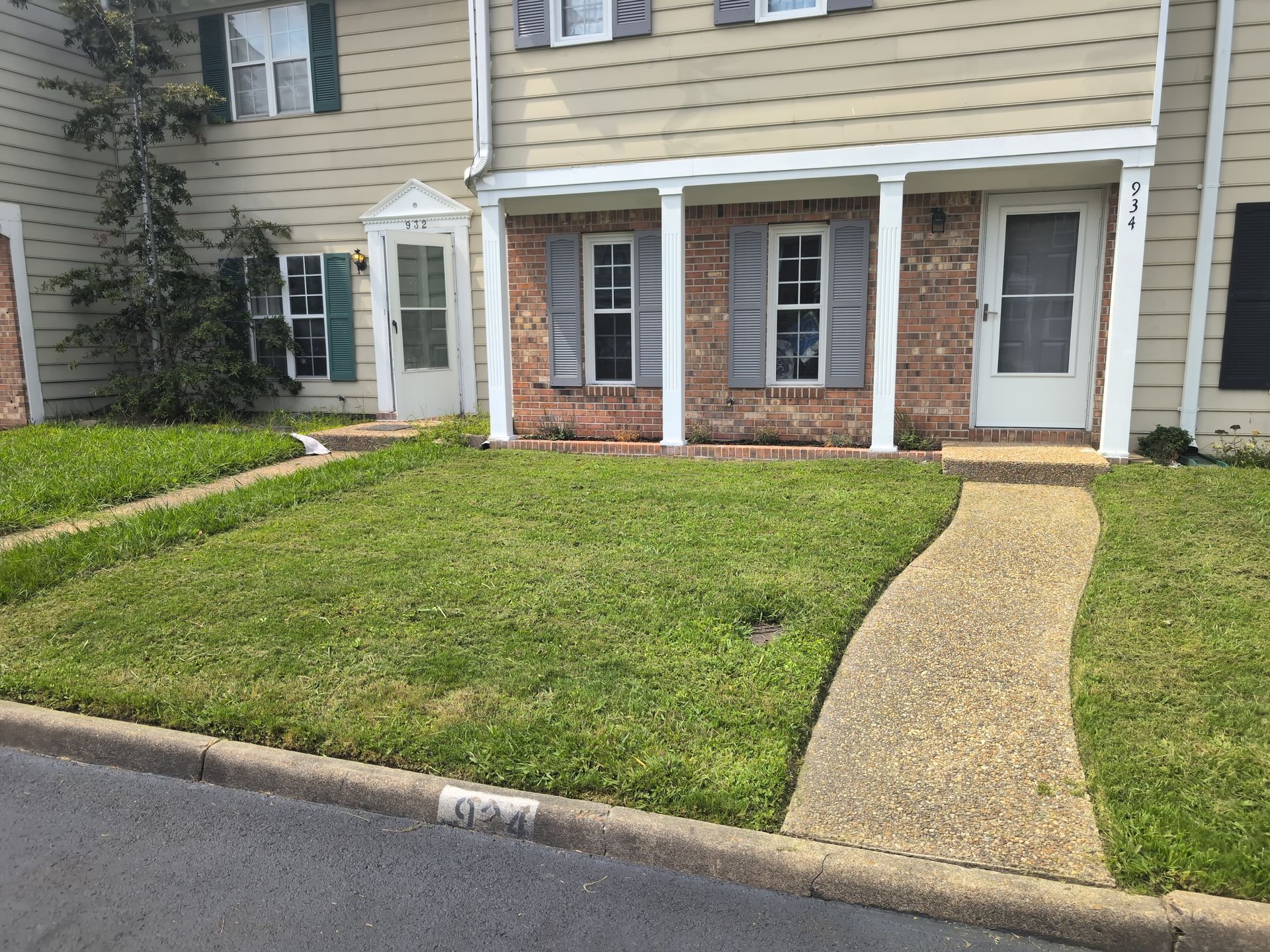 Townhouse front with brick columns, tan siding, a green lawn, and a curved concrete walkway to the door
