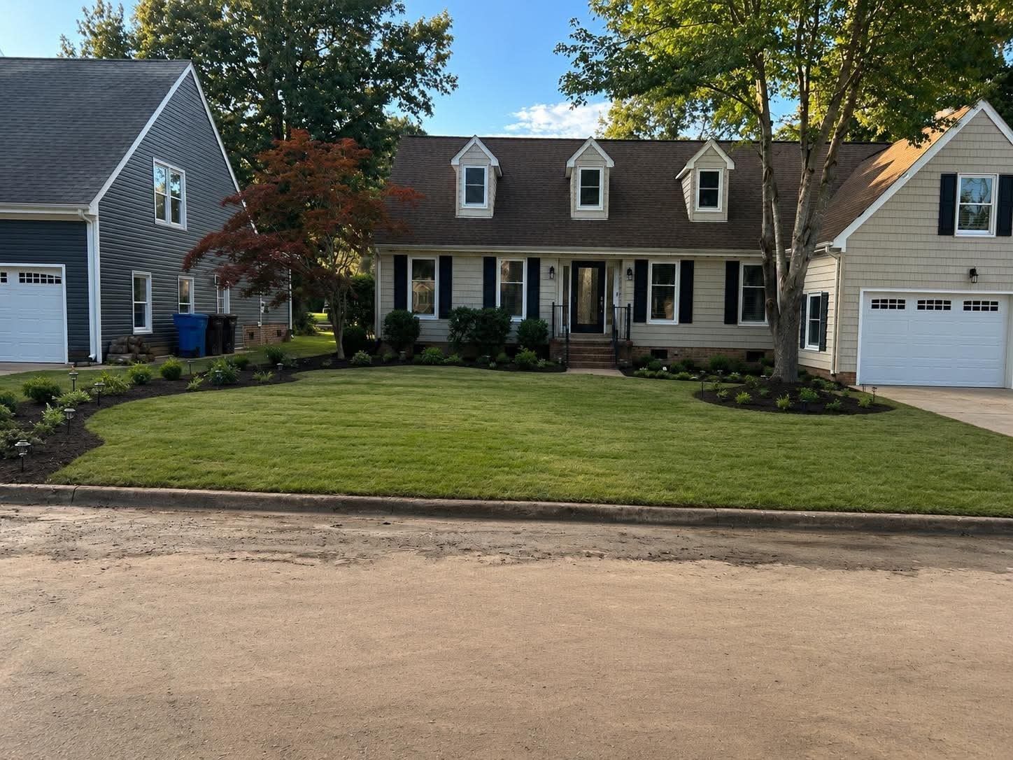 Suburban house with gray siding, white trim, a large lawn, and a detached garage under trees