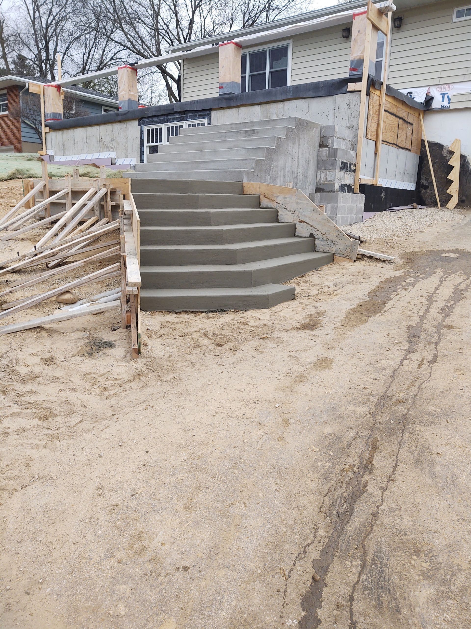Curved concrete steps leading to a stone patio and house under construction, with siding and scaffolding visible.